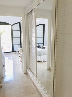 A hotel room with a large sliding glass door leading to a balcony, a bed with a gray and white bedspread, and a small seating area with a chair and table.