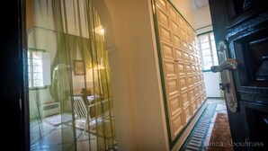 Un couloir avec une porte en verre, une porte en bois ornée d’un motif à croisillons et une porte en bois foncé avec une poignée en laiton.