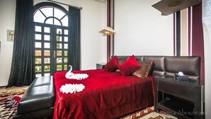 Une chambre d’hôtel avec un grand lit, une banquette, une table de chevet et une fenêtre avec des rideaux.