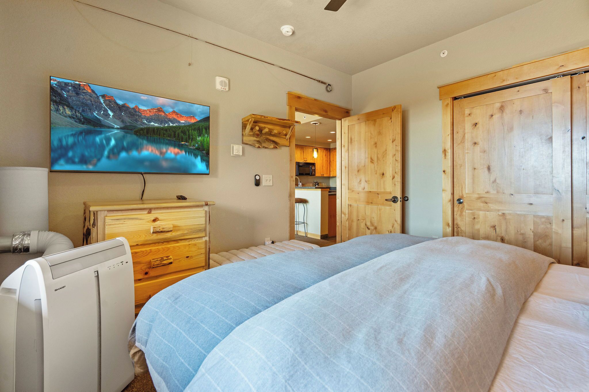 A bedroom with a large bed, a dresser, a TV mounted on the wall, and a wooden door.