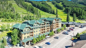 A multi-story lodge with a green roof, surrounded by a parking lot and a mountainous landscape.