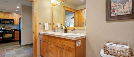 A bathroom with wooden cabinets, a double sink, a large mirror, and a toilet with toilet paper.