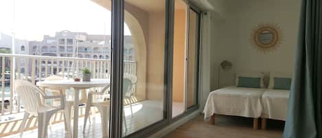 A balcony with a table and chairs, a bed with a view of the city, and a large window.