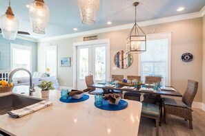 A modern kitchen with a central island, dining area with wicker chairs, and a hanging light fixture. - Heated Private Pool*, Walk to the Beach! Golf Cart & 6 Bikes! - Blue Dune 30A in Blue Mountain Beach (Santa Rosa Beach)