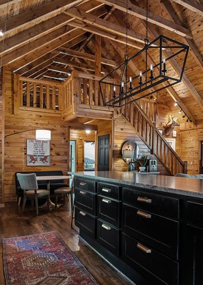 A spacious log cabin interior with a high ceiling, a central staircase, a dining area with a table and chairs, and a kitchen with a large island. - Boat Days Begin Here, Walk to  Hurricane Marina (silver point)