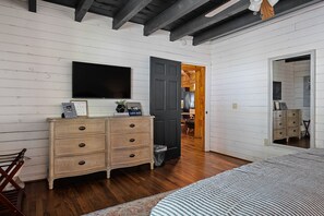 Een slaapkamer met een bed, een dressoir, een televisie en een deur die naar een andere kamer leidt.