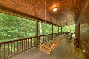 A wooden deck with a hanging bench and a table, overlooking a forested area. - Ole Bear Paw Cabin - Cherry Log (Cherry Log)