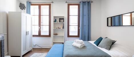A bedroom with a bed, a wardrobe, a small shelf, and a window with curtains.