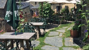 Un espace extérieur aménagé en terrasse, avec des allées en pierre, des tables en bois et des chaises en métal vert.