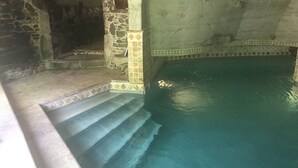 Une piscine aux murs en pierre, bordée de carreaux et dotée d’une petite fenêtre.