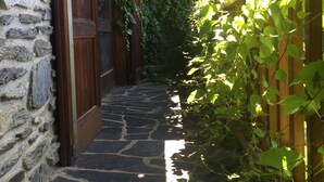 Un étroit sentier de pierres mène à une porte en bois dotée d’une poignée en métal, le tout étant entouré d’un feuillage verdoyant et luxuriant.