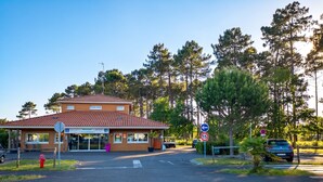 A building with a tiled roof, a signboard, and a parking area with cars. - Homerez - House in Parentis-en-Born (Parentis-en-Born)