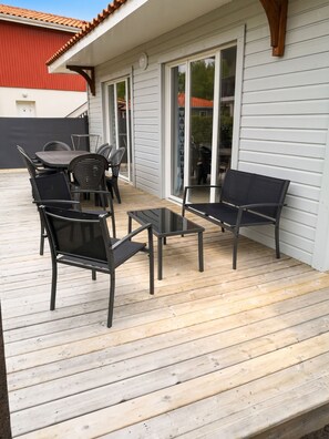 A covered outdoor patio with a table and chairs, a sliding glass door, and a wooden deck. - Homerez - House in Parentis-en-Born (Parentis-en-Born)