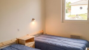 A room with two beds, a small wooden desk, a wall-mounted light, and a window with a view of a building outside. - Homerez - House in Parentis-en-Born (Parentis-en-Born)