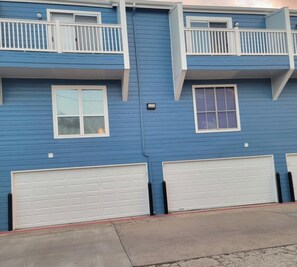 Een woonhuis met twee verdiepingen, een blauwe gevel, witte garage deuren en een balkon met witte leuningen.