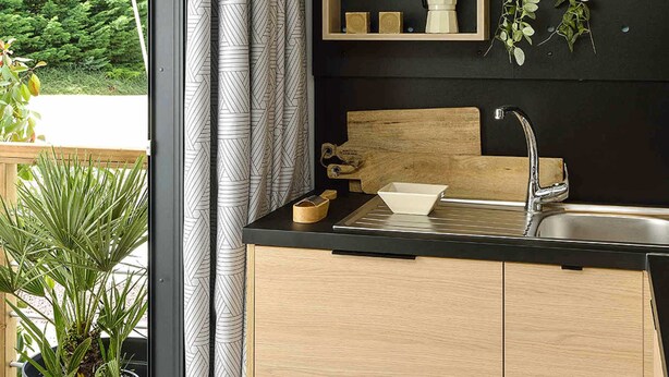 A modern kitchen with a black countertop, wooden cabinets, a stainless steel sink, and a window with curtains. - St Maurice - Plein Air Chalet C1 (Dieulefit)