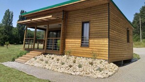 A wooden cabin with a green roof, a covered porch, and a gravel pathway leading to the entrance. - St Maurice - Plein Air Chalet C1 (Dieulefit)