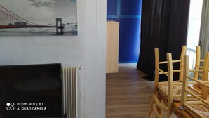 A room with a bed, a radiator, a painting of a bridge, a blue wall, and a window with curtains. - Studio by the sea (La Grande-Motte)