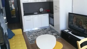 A compact living space with a kitchenette, a dining area with a small table and chairs, and a television on a stand. - Studio by the sea (La Grande-Motte)