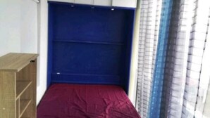 A small, single-bed room with a blue headboard, a wooden nightstand, and a window with blue curtains. - Studio by the sea (La Grande-Motte)
