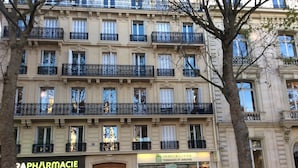 A multi-story building with a pharmacy on the ground floor, a real estate agency on the second floor, and balconies with wrought iron railings.