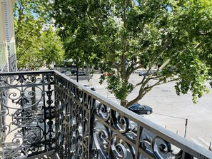 Ein Balkon mit aufwendigen Metallgeländern, der auf eine Straße mit Autos und Bäumen blickt.