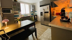 A modern kitchen with a dining area, featuring stainless steel appliances, a wooden table, and a bench.
