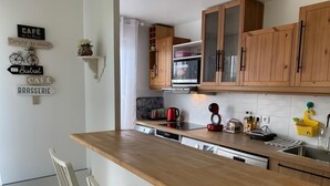 A kitchen with wooden cabinets, a microwave, a coffee maker, and a sink. There are signs on the wall and a chair in the corner.
