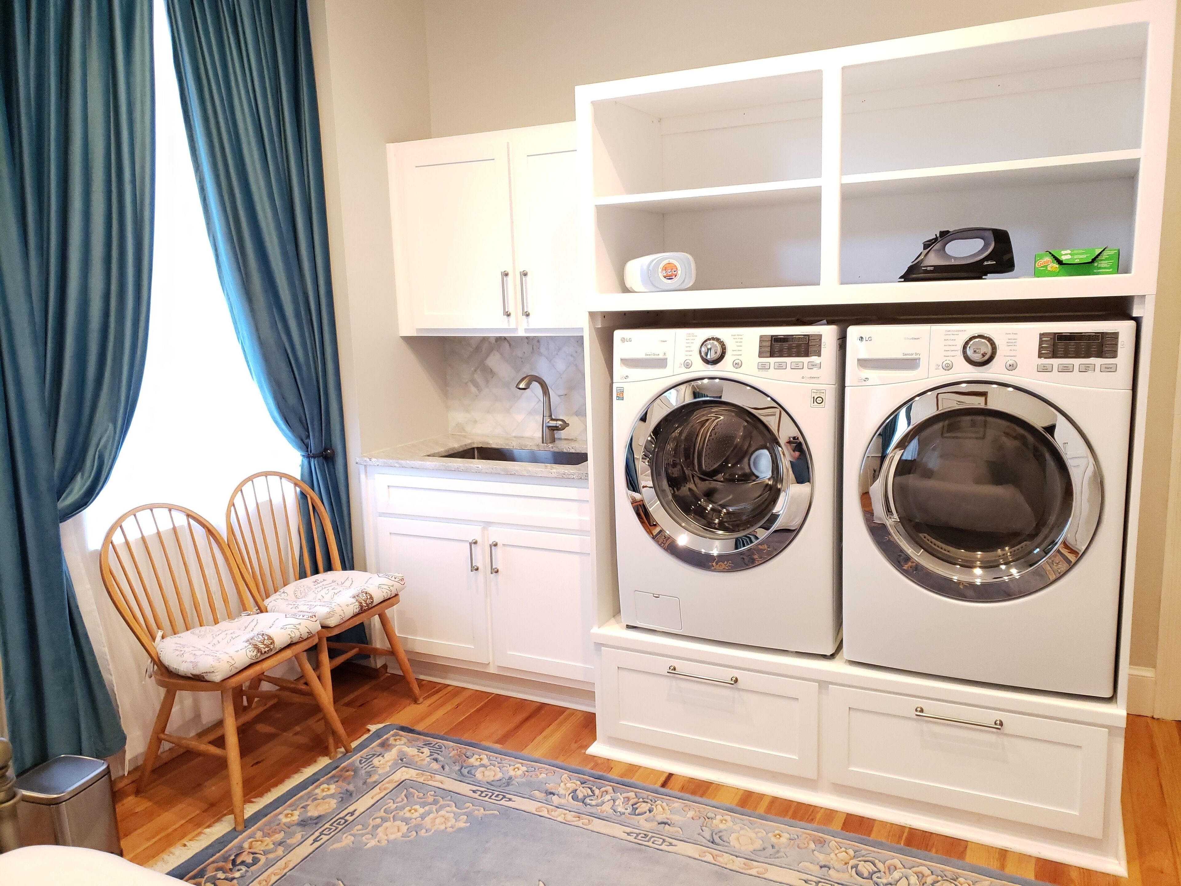 A laundry room with two front-loading washing machines, a sink, and a chair.