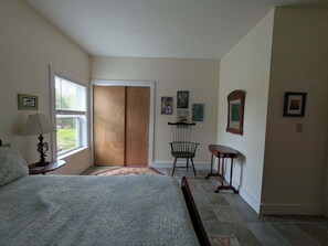 Une chambre à coucher comprenant un lit, une table de chevet, une lampe, une armoire en bois, une chaise, une petite table et un miroir.