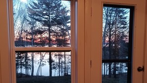 Une vue à travers une fenêtre, avec le reflet des arbres et d’un coucher de soleil.