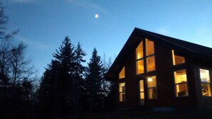 Une cabane dotée de grandes fenêtres et d’un toit en pente, entourée d’arbres.