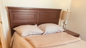 A neatly made bed with a patterned bedspread and pillows, a wooden headboard, and a bedside lamp. - DENIS TEMPORARY HOUSING 3 BEDROOMS APT- D (Killeen)