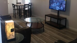 A living room with a TV, a ceiling fan, a dining area with chairs, and a lamp. - DENIS TEMPORARY HOUSING 3 BEDROOMS APT- D (Killeen)