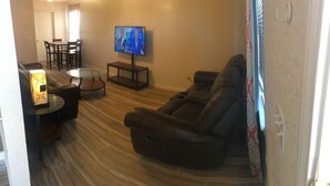 A living room with a leather sofa, a glass coffee table, a TV on the wall, and a small side table. - DENIS TEMPORARY HOUSING 3 BEDROOMS APT- D (Killeen)