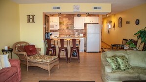 Ein Wohnzimmer mit einer Couch, Sesseln, einem Essbereich mit Tisch und Stühlen sowie einer Küche mit Schränken und Geräten.