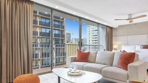 A modern hotel room with a large window, a sofa, a coffee table, and a round ottoman.