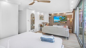 A modern hotel room with a bed, a sofa, a ceiling fan, a TV, and a view of the outdoors.
