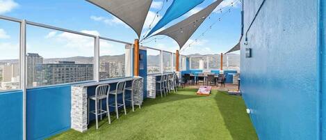 A rooftop bar with a view of the city, green artificial turf, and blue walls.