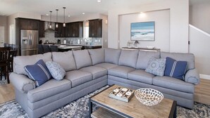 Un salon moderne avec un canapé d’angle gris, une table basse et une cuisine en arrière-plan.