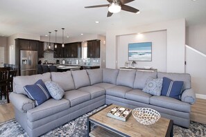A modern living room with a grey sectional sofa, a coffee table, and a kitchen in the background.