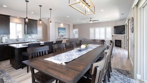 Une cuisine spacieuse dotée d’un îlot central, de luminaires suspendus et d’un coin repas avec une longue table.