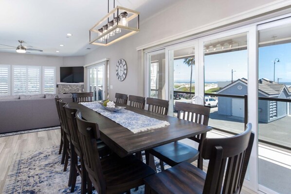 A dining area with a dark wooden table, multiple chairs, a chandelier, and a view of the outside through large sliding glass doors.