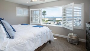 Une chambre avec un grand lit, un ventilateur de plafond, une vue sur la plage et une fenêtre équipée de stores.
