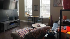 A living room with a flat-screen TV, a round dining table with chairs, a sofa, and a window with blinds. - The "Zen" unit is a tranquil environment,  In the middle of everything & relax! (Knoxville)