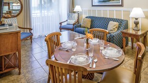 Enjoy dining and relaxation in this inviting space with a round table for four, a blue patterned sofa, and a wooden desk.