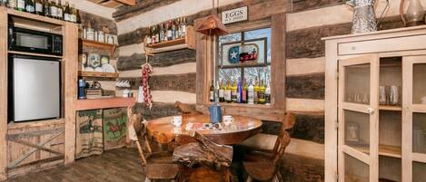 A rustic wooden interior with a wooden table, chairs, a refrigerator, a microwave, and a cabinet with glass doors.