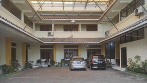 A covered courtyard with two cars parked, potted plants, and a building with multiple windows and doors.