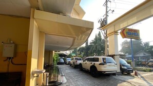 A hotel entrance with a covered area, a bench, a sink, and a row of parked cars.