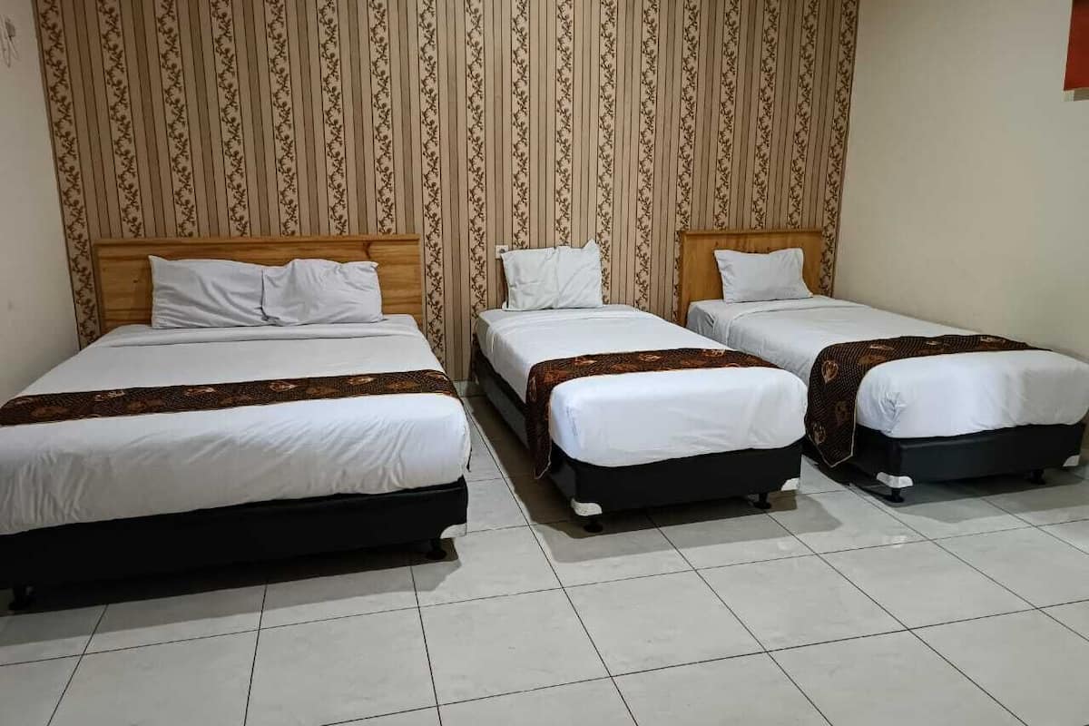 A hotel room with three single beds, each with a wooden headboard and white bedding. The room has a tiled floor and a patterned wallpaper on the wall.